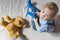 Cute baby boy and his teddy bear watching TV sitting on a couch in the living room at home, top view