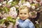 Cute baby boy among pink blossoming flowers