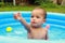 Cute baby boy reaching for something in blue inflating pool