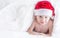 Cute baby boy with santa hat on bed under white duvet