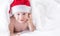 Cute baby boy with santa hat on bed under white duvet