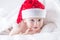 Cute baby boy with santa hat on bed under white duvet