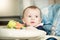 Cute baby boy sitting in child chair with table