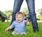 Cute Baby Boy Sitting In Front Of Mother In Park