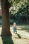 Cute baby boy standing under huge large tree in park on sunset. Adorable smiling child one year old toddler walking outdoors on