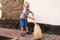 Cute baby boy sweeps the yard with a broom, mother assistant