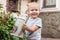 Cute baby boy waters the flowers on the back yard, mother assistant.