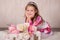 Cute baby girl with brunette hairs pink cheeks and green eyes posing sit for camera in studio wearing airy colourful dress and fan