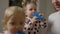 Cute baby girl drinking multivitamin juice with twin sister and mother at home. Portrait of charming pretty Caucasian