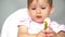 Cute baby girl holding a spoon with vegetables. A child studies spoon, vegetables fall from spoon on table.