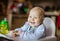 Cute baby girl sitting in high chair and eating piece of bread