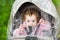 Cute baby girl sitting in stroller under plastic rain