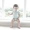 Cute baby at home in white room is sitting near window. The beautiful baby could be a boy or girl and is wearing body suit.