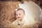 Cute baby newborn child posing in huge broken egg on dry straw in unique studio design decoration