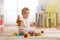 Cute baby playing with colorful toys sitting on carpet in white sunny bedroom. Child with educational toys. Early