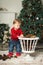 Cute baby plays with cones to decorate the Christmas tree, takes them out of the basket. Near the Christmas tree and boxes with