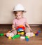 Cute baby in protective helmet playing with plastic constructor