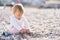 Cute baby sits on a pebble beach and digs a hole