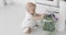 A cute baby sits on a white floor and plays with a decorative cage.