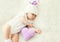 Cute baby sleeping on white bed at home with knitted pillow heart