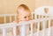 A cute baby is standing in the crib and biting the railing. teeth eruption concept