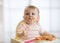 Cute baby toddler girl eating spaghetti with tomato sauce sitting in a white sunny room with big window