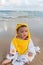 Cute baby wearing a yellow cartoon bathrobe sitting and playing on the beach near the sea
