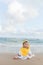 Cute baby wearing a yellow cartoon bathrobe sitting and playing on the beach near the sea