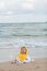 Cute baby wearing a yellow cartoon bathrobe sitting and playing on the beach near the sea