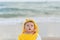 Cute baby wearing a yellow cartoon bathrobe sitting and playing on the beach near the sea