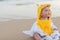 Cute baby wearing a yellow cartoon bathrobe sitting and playing on the beach near the sea