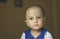 Cute bald indian baby boy in blue and white shirt looking away. Head and shoulder shot. Close up