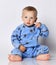 Cute barefooted blond baby boy toddler in blue fleece jumpsuit with stars sits on the floor touching his ear, pointing