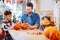 Cute beaming son wearing Halloween costume carving pumpkin with his father