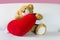 Cute bear doll sit with red heart on sofa and pink background