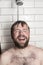 Cute bearded man standing in the shower under running water and
