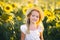 Cute beatiful little girl in light clothes and a big straw hat on a field of sunflowers