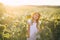 Cute beatiful little girl in light clothes and a big straw hat at sunset on a field of sunflowers