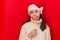 Cute beautiful brunette girl in Santa hat smiles and poses with false paper lips isolated on red background