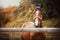 A cute, beautiful sorrel horse with a halter on its muzzle stands in a paddock with a wooden fence on a farm on an autumn day.