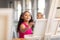 Cute biracial elementary schoolgirl painting on easel during drawing class in school