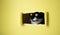 Cute black kitten with a white muzzle peeks into a rectangular hole on a yellow background