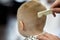 Cute blond baby boy in a barber shop having haircut by hairdresser. Hands of stylist with hairbrush.