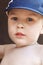 Cute blond baby boy with bright blue eyes in blue cap. Emotion of fun, joy, attention.