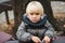 Cute blond baby boy playing with toys outdoors. Toddler boy with blue eyes and blonde hair. Child in warm jacket at walk in cold