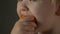 Cute blond baby is eating raw carrots to reinforce his vision. Delicious vegetarian food
