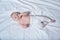 Cute blond baby with fingers in his mouth lies on a white sheet. Top view