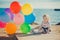 Cute blond baby girl child posing enjoying summer life time on sandy beach sea side on wooden pier with colourful plenty balloons