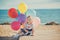 Cute blond baby girl child posing enjoying summer life time on sandy beach sea side on wooden pier with colourful plenty balloons