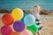 Cute blond baby girl child posing enjoying summer life time on sandy beach sea side on wooden pier with colourful plenty balloons